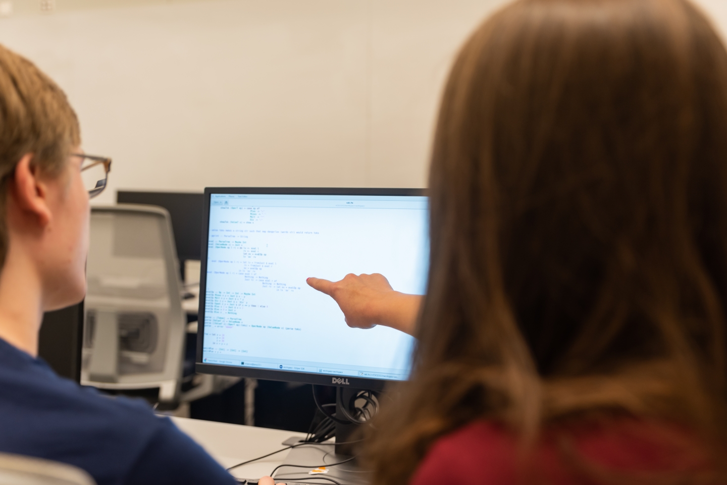 one student pointing at computer screen as other student looks on