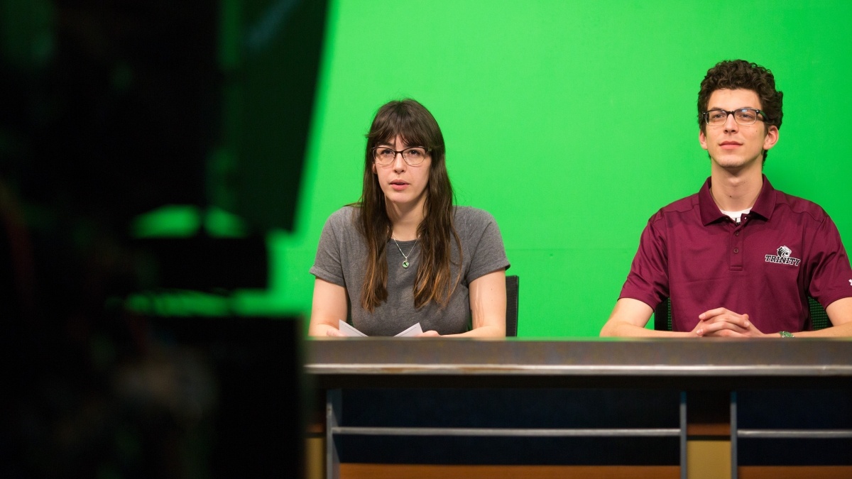 Students sitting in front of a teleprompter in front of the green screen