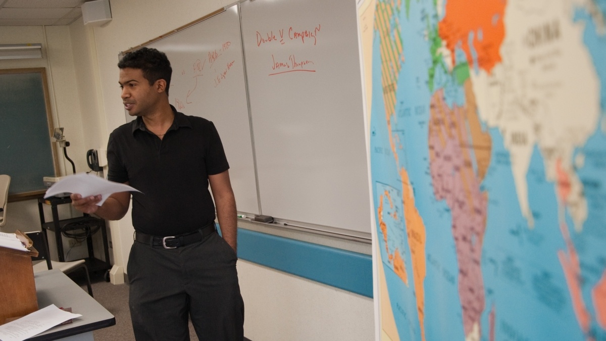 Professor teaching next to whiteboard and map of the world
