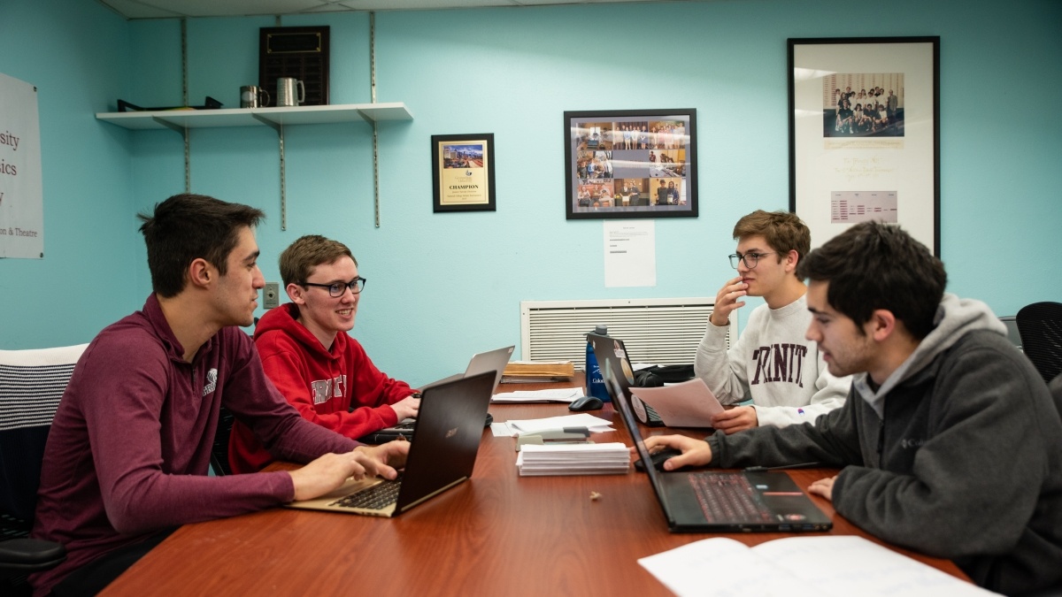 Group of students meeting around a desk with their laptops open