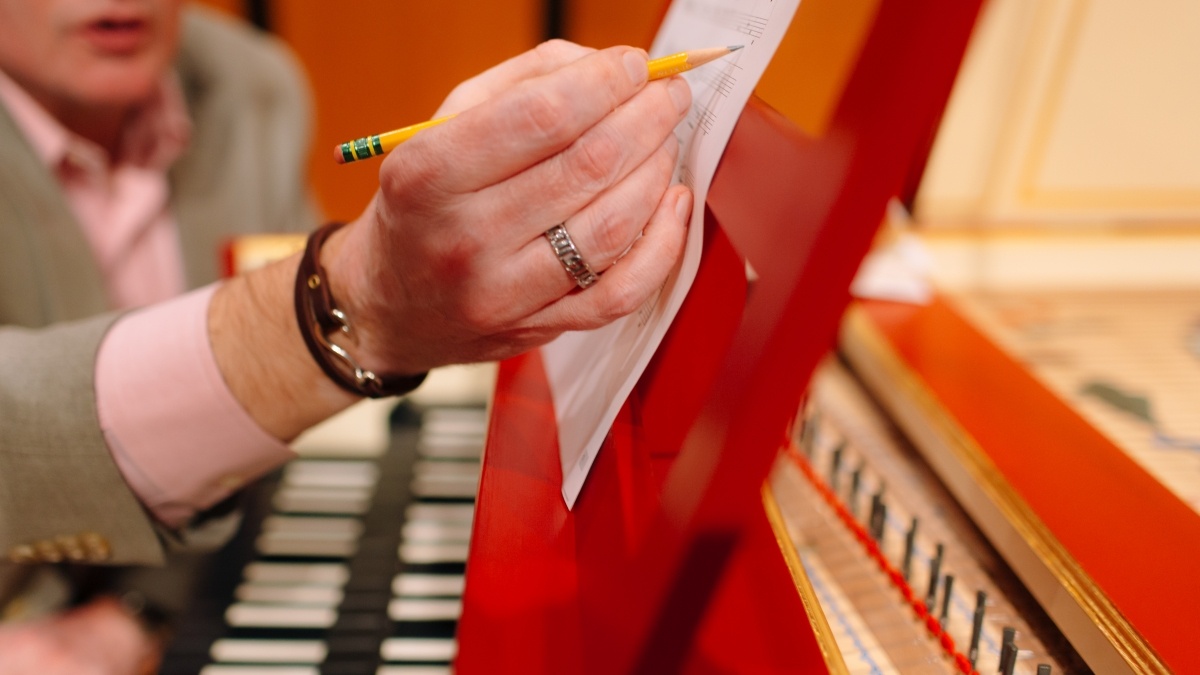Person marking sheet of music while on harpsichord