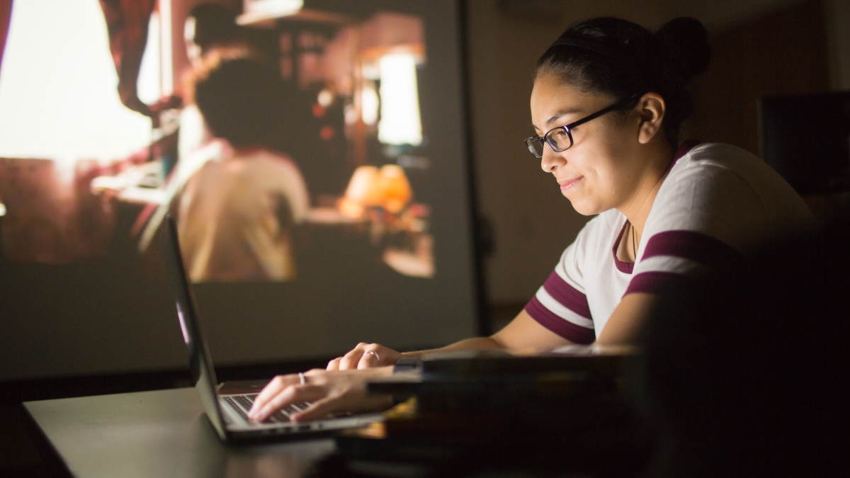 Woman typing on computer as movie plays in the background