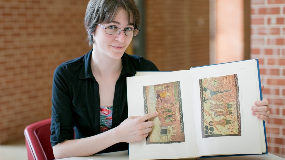 A student displays a book with ancient art