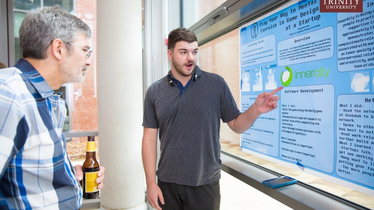 A student points toward code for a game while an onlooker observes. 