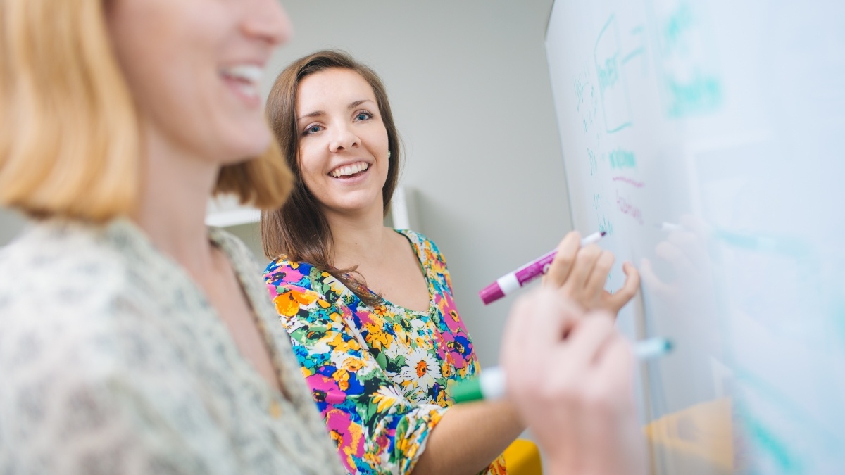 two people writing on a white board with colored markers