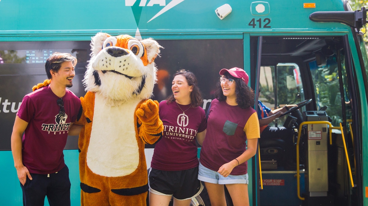three students and the LeeRoy mascot stand in front of the VIVA culture bus